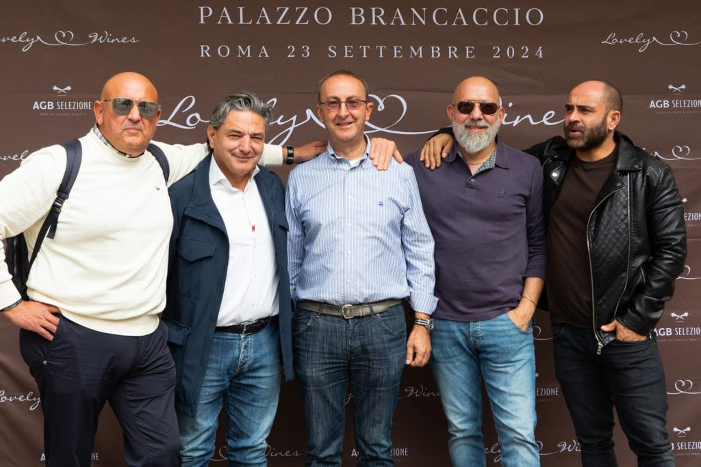 Cinque uomini posano insieme davanti a uno sfondo di marca a Palazzo Brancaccio a Roma, il 23 settembre 2024. Sono sorridenti, vicini e vestiti con abiti casual e smart-casual.