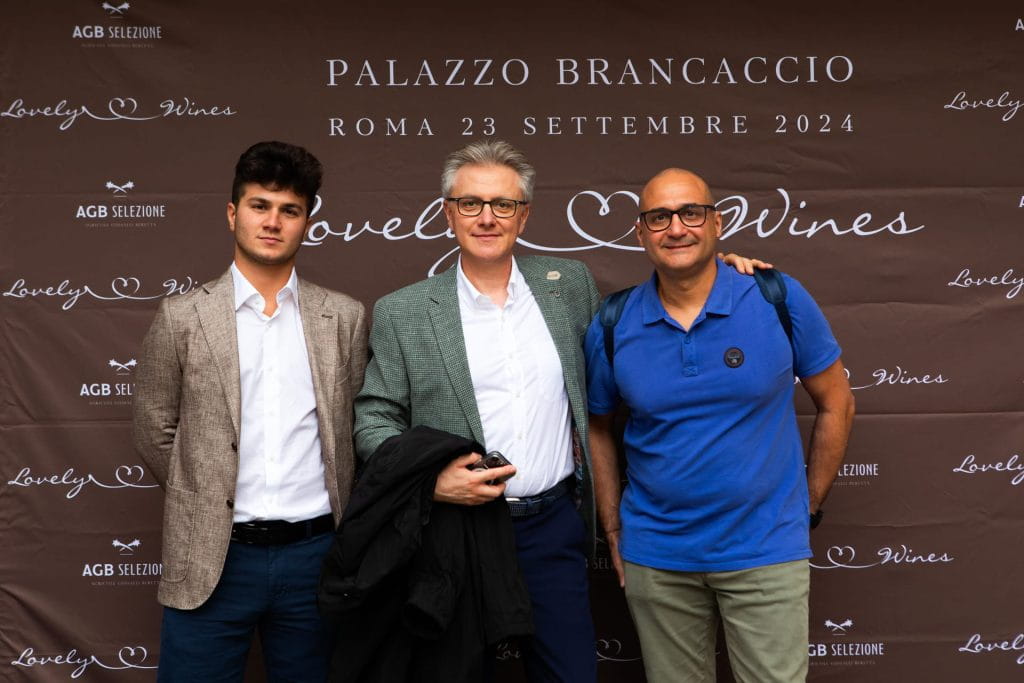 Tre uomini insieme in posa per una foto davanti a un fondale con la scritta Palazzo Brancaccio, Roma 23 settembre 2024, Lovely Wines. Sono vestiti in modo semi-formale e casual.