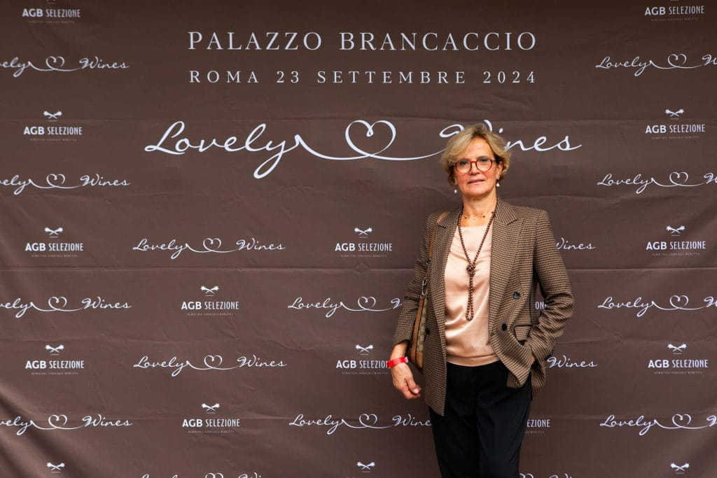 Una donna in abito da lavoro si trova davanti a un fondale marrone con testo bianco che promuove Lovely Wines a Palazzo Brancaccio, Roma, il 23 settembre 2024.