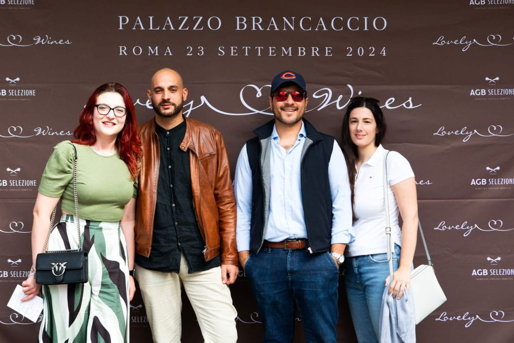 Quattro persone posano insieme davanti a uno sfondo di marca durante un evento a Palazzo Brancaccio a Roma il 23 settembre 2024. Sono vestite in abiti eleganti e sorridono alla macchina fotografica.