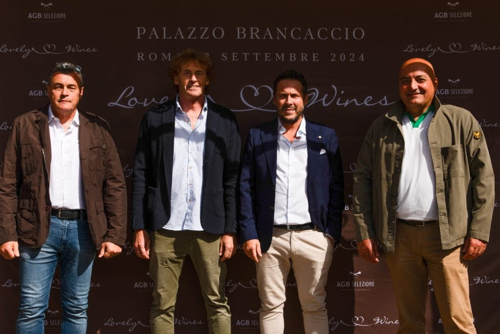 Quattro uomini affiancati, sorridenti, davanti a un fondale con la scritta Palazzo Brancaccio, Roma, Settembre 2024, Lovely Wines. Sono vestiti con abiti casual e smart-casual.