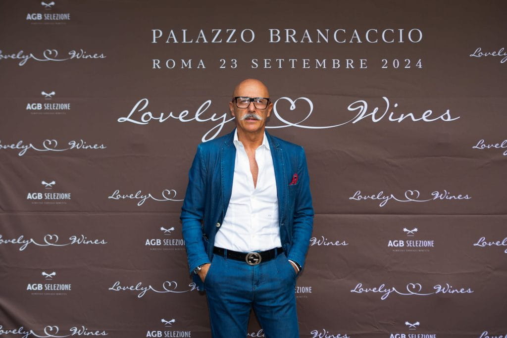 Un uomo in abito blu si trova davanti a un fondale marrone con le scritte Lovely Wines, Palazzo Brancaccio e Roma 23 Settembre 2024.