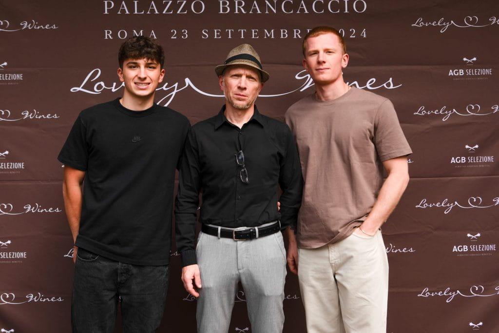 Tre uomini sono insieme davanti a un fondale marrone con scritte in corsivo e dettagli dell'evento, tra cui Palazzo Brancaccio, Roma 23 Settembre 2024 e Lovely Wines.
